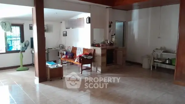 Spacious open-plan living area with tiled flooring and natural light, featuring a cozy seating area and kitchen space.