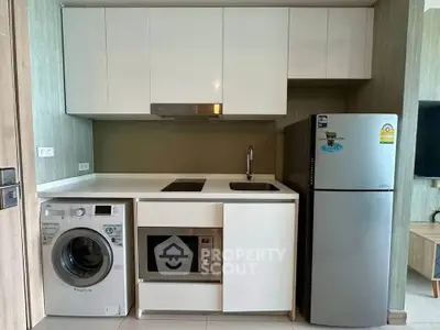 Modern kitchen with sleek appliances including washing machine, microwave, and fridge in compact layout.