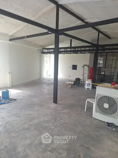 Spacious industrial-style open space with exposed beams and concrete flooring, ideal for creative office or studio.