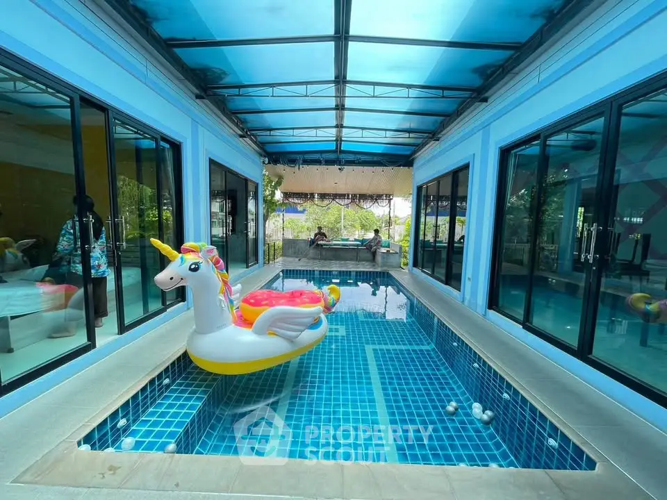 Luxurious indoor pool with unicorn float in modern home, featuring glass doors and vibrant blue tiles.