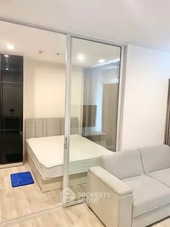 Modern studio apartment with glass partition, cozy bed, and comfortable sofa.