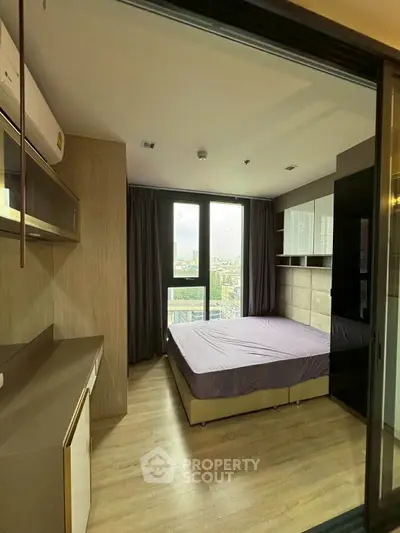 Modern bedroom with large window and city view, featuring sleek furniture and wooden flooring.