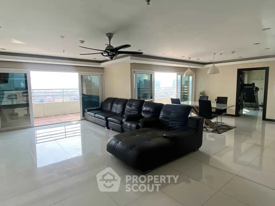 Spacious modern living room with leather sofas and city view balcony.