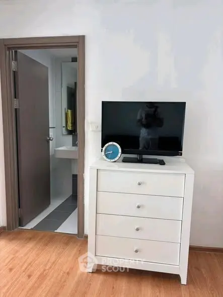 Modern bedroom with sleek dresser and TV, adjacent to a stylish bathroom.