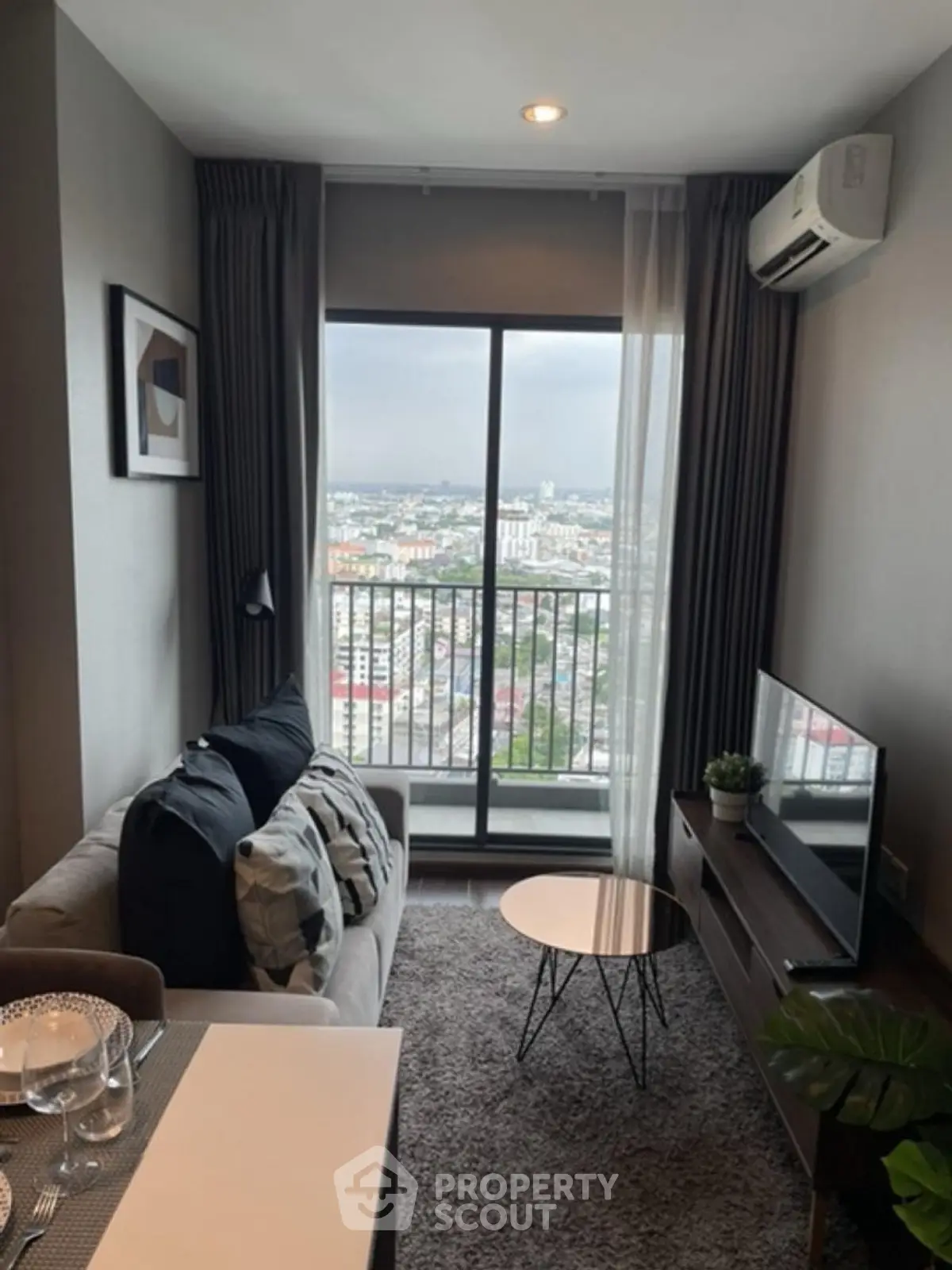 Modern living room with city view, cozy sofa, and stylish decor in high-rise apartment.