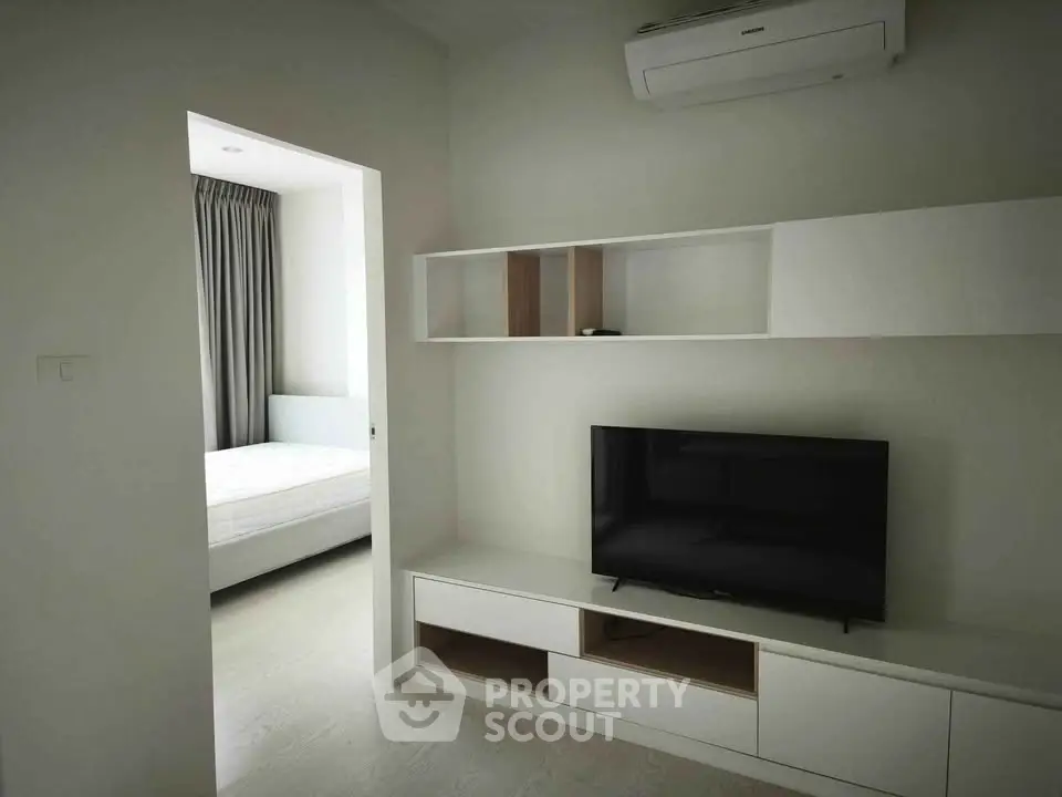 Modern living room with sleek TV unit and view into a cozy bedroom, featuring minimalist design and air conditioning.