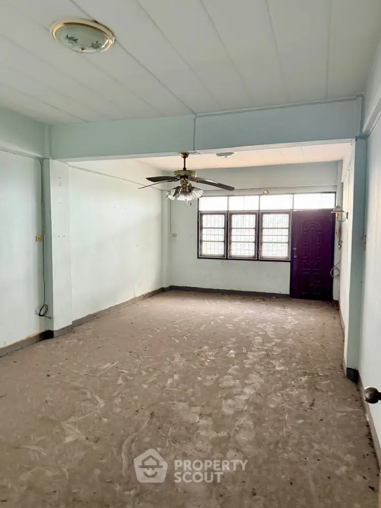 Spacious empty room with ceiling fan and large windows, ready for customization.