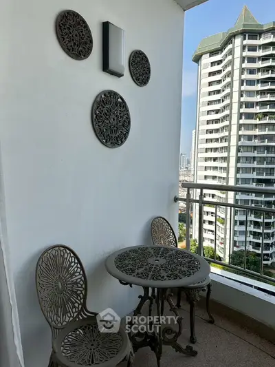 Charming balcony with ornate metal furniture and city view in modern high-rise apartment.