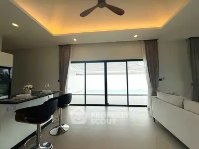 Modern living room with open layout and pool view, featuring stylish bar stools and elegant ceiling lighting.