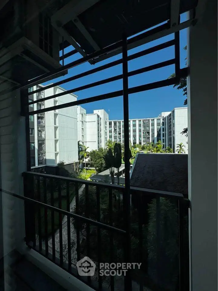Modern apartment complex view from balcony with lush garden and clear blue sky.