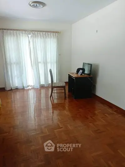 Spacious room with parquet flooring and natural light, ideal for home office setup.