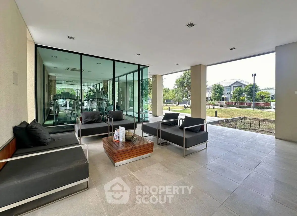 Modern outdoor seating area with glass-walled gym and garden view, perfect for relaxation.