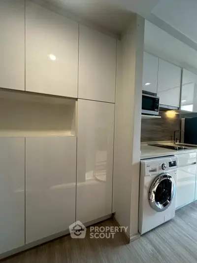 Modern kitchen with sleek white cabinets and built-in appliances, featuring a washing machine and microwave.