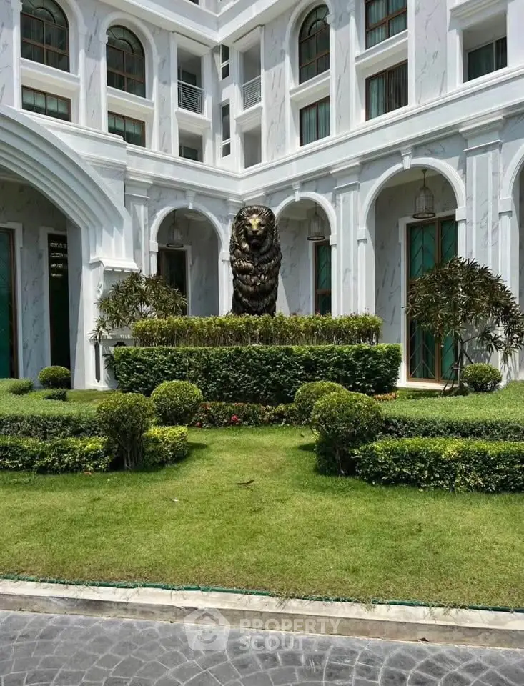 Elegant building facade with manicured garden and lion statue, showcasing luxury architecture.