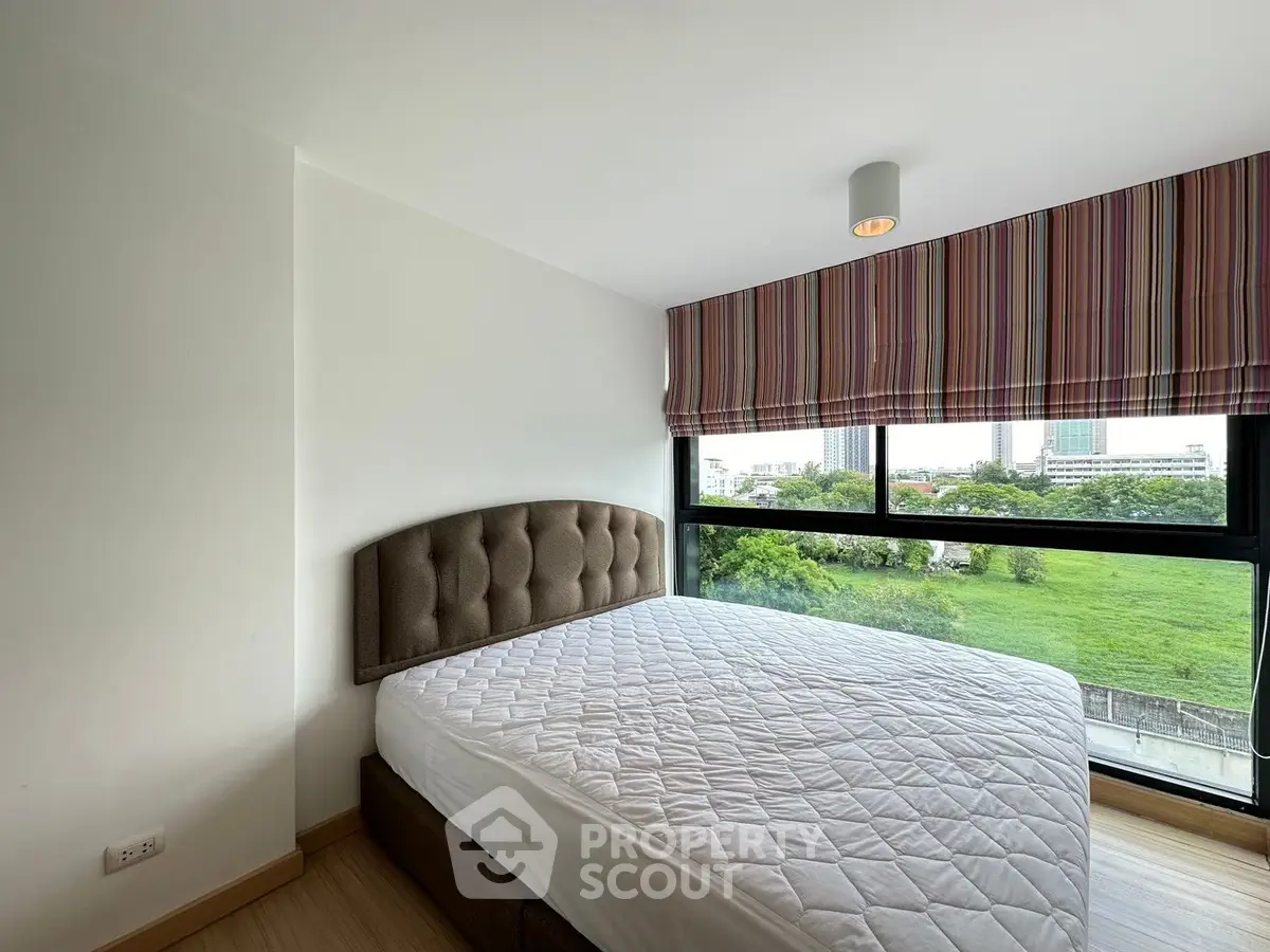 Cozy bedroom with large window offering lush green view, modern decor, and natural light.