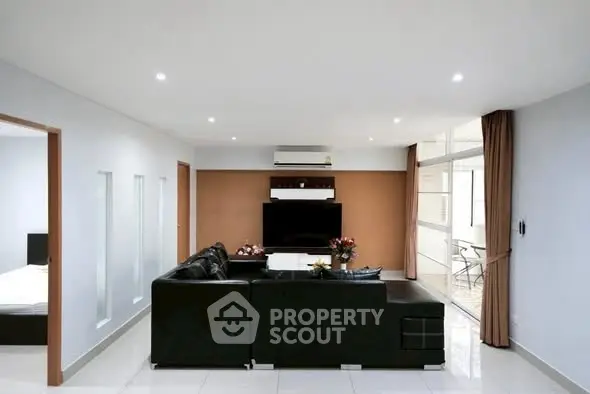 Spacious modern living room with sleek black sofa and large TV, ideal for entertainment.