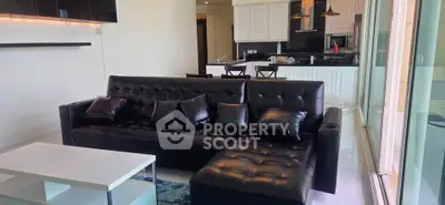 Modern open-layout living room with sleek black leather sofa and stylish kitchen area.