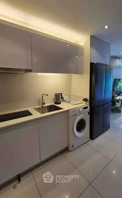 Modern kitchen with sleek cabinets, washing machine, and stainless steel fridge.