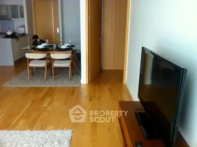 Modern living room with dining area and sleek wooden flooring, featuring a flat-screen TV and stylish furniture.