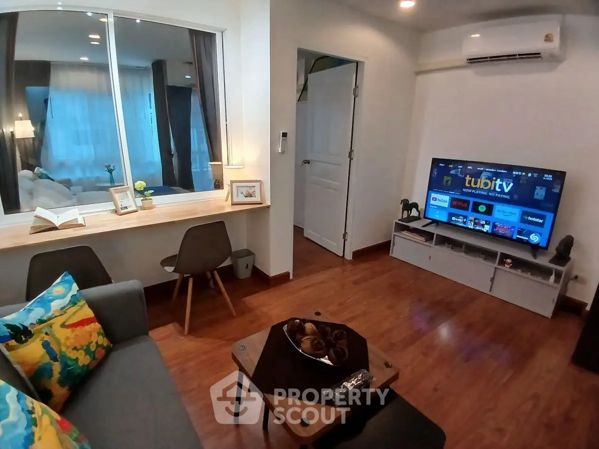 Cozy living room with modern decor, featuring a wall-mounted TV, stylish furniture, and a large window for natural light.