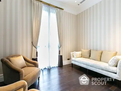 Elegant living room with polished hardwood floors, plush seating, and floor-to-ceiling curtains, bathed in natural light.