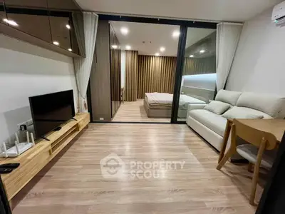 Modern living room with wooden flooring, sleek furniture, and a view into a cozy bedroom.