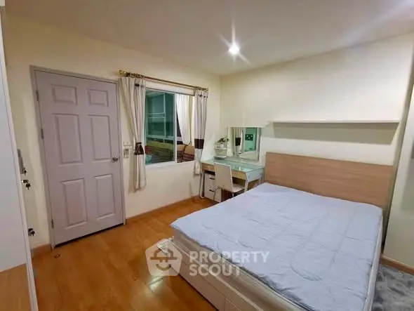 Cozy bedroom with wooden flooring and modern furnishings in a well-lit apartment.