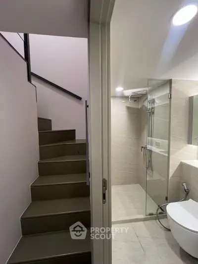 Modern bathroom with glass shower and adjacent staircase in sleek apartment