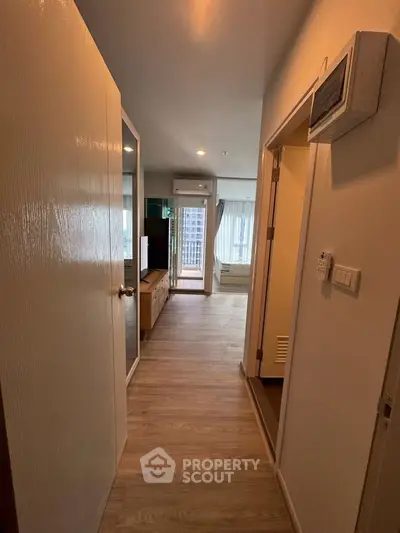 Modern apartment hallway with wooden flooring leading to a bright living area with large windows.