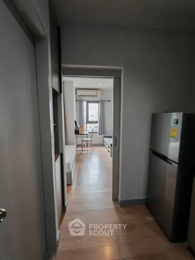 Modern apartment hallway leading to a bright bedroom with wooden flooring and natural light.