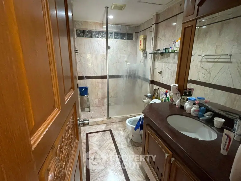 Luxurious marble bathroom with glass shower and elegant wooden cabinetry.