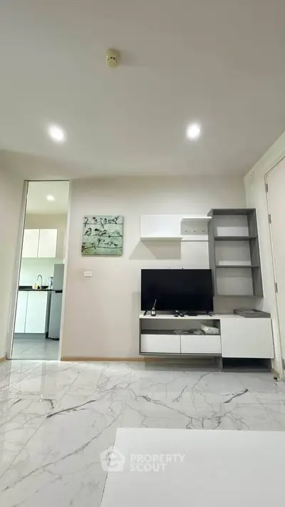 Modern living room with sleek marble flooring and stylish TV unit, adjacent to a contemporary kitchen.