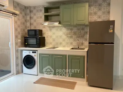 Modern kitchen with green cabinets, washing machine, and fridge in stylish apartment.