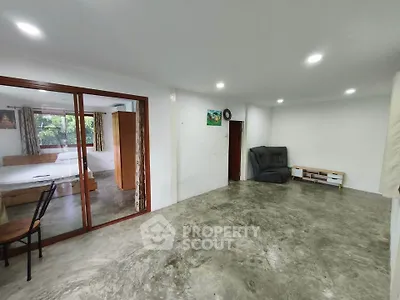 Spacious living area with concrete flooring and sliding glass doors leading to a bedroom.
