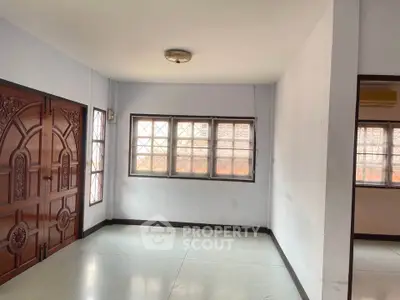 Spacious empty room with elegant wooden door and large windows, perfect for customization.