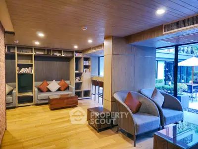 Spacious modern living room with elegant grey sofas, hardwood floors, and a cozy reading nook by the window overlooking a serene outdoor patio.