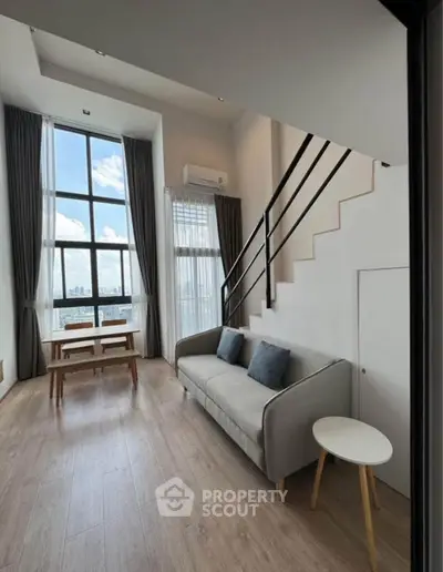 Modern loft-style living room with high ceilings and large windows offering a stunning city view.