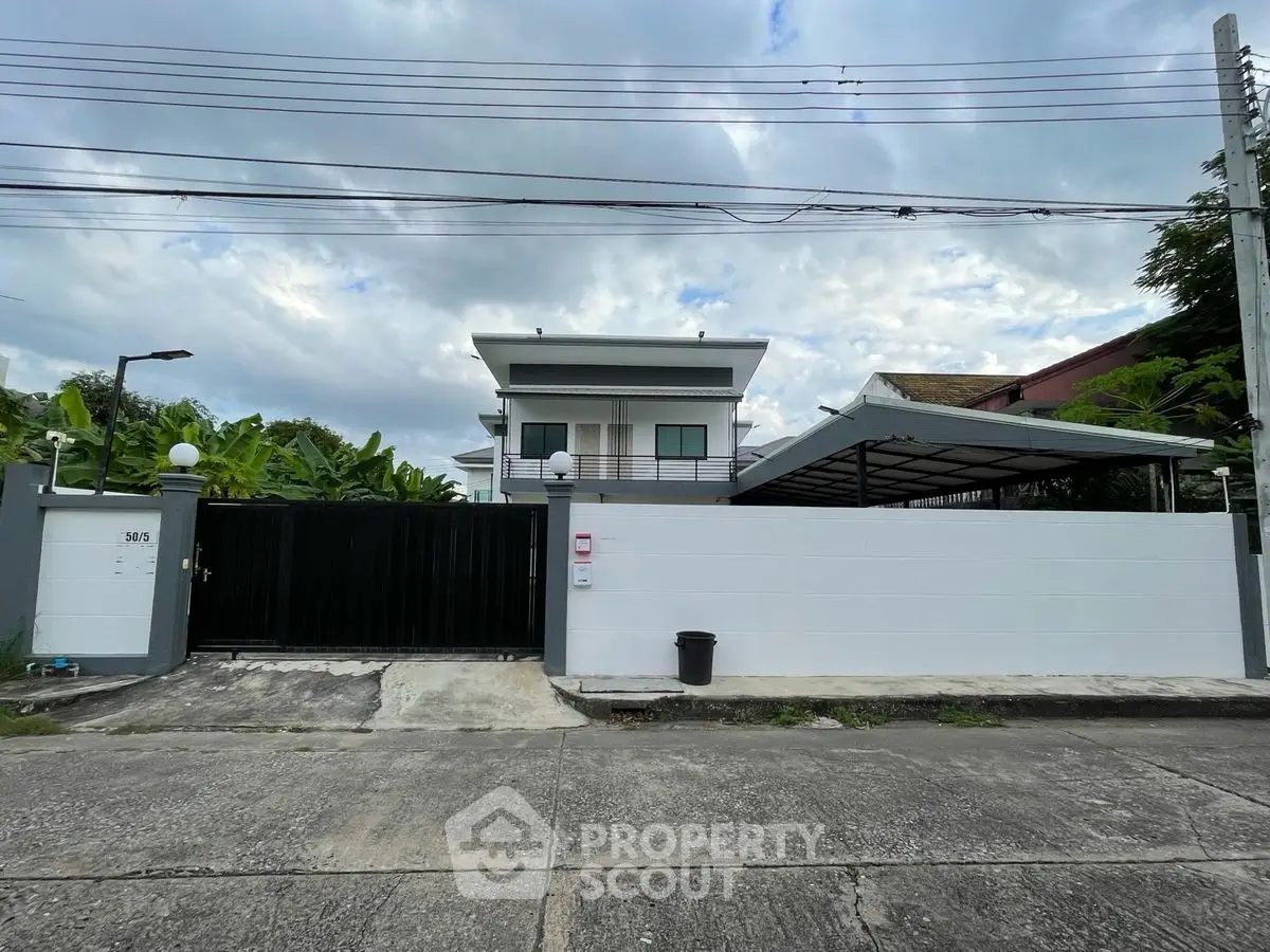Modern two-story house with gated entrance and carport in suburban setting.