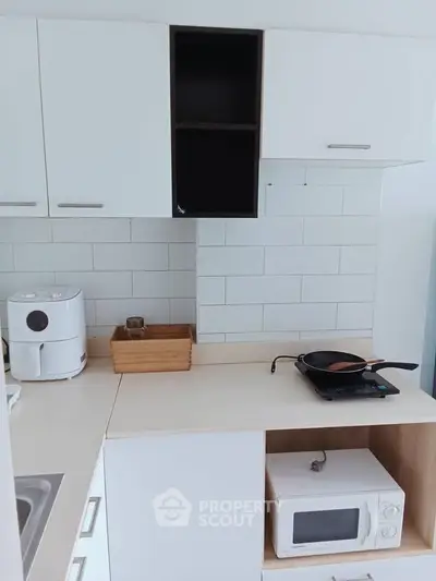 Modern kitchen with sleek white cabinets and compact appliances, perfect for efficient cooking.