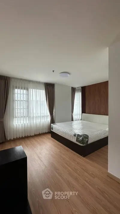 Spacious bedroom with large windows and wooden flooring in modern apartment.