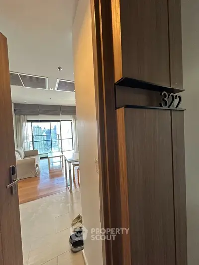 Modern apartment entrance with open door revealing stylish living room and city view.