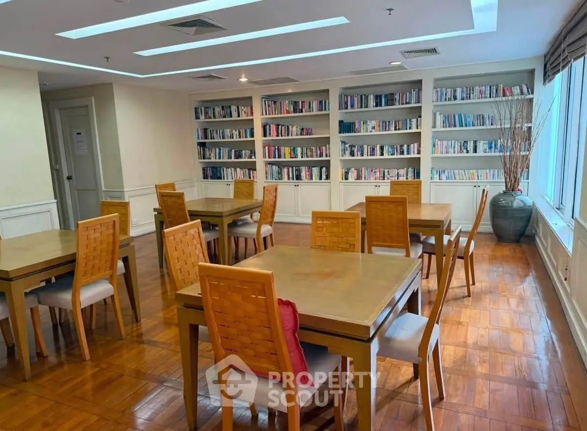 Elegant library with wooden tables and chairs, surrounded by bookshelves and natural light.