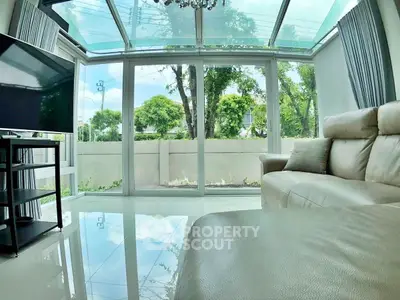 Spacious living room with glass walls and modern furniture, offering a serene garden view.