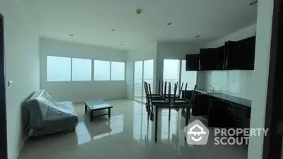 Spacious open-layout living room with modern kitchen and large windows offering natural light.