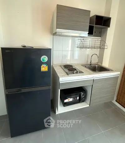 Compact modern kitchen with fridge, microwave, and electric stove in a sleek apartment setting.