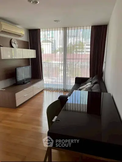 Modern living room with sleek furniture and large window offering city views.