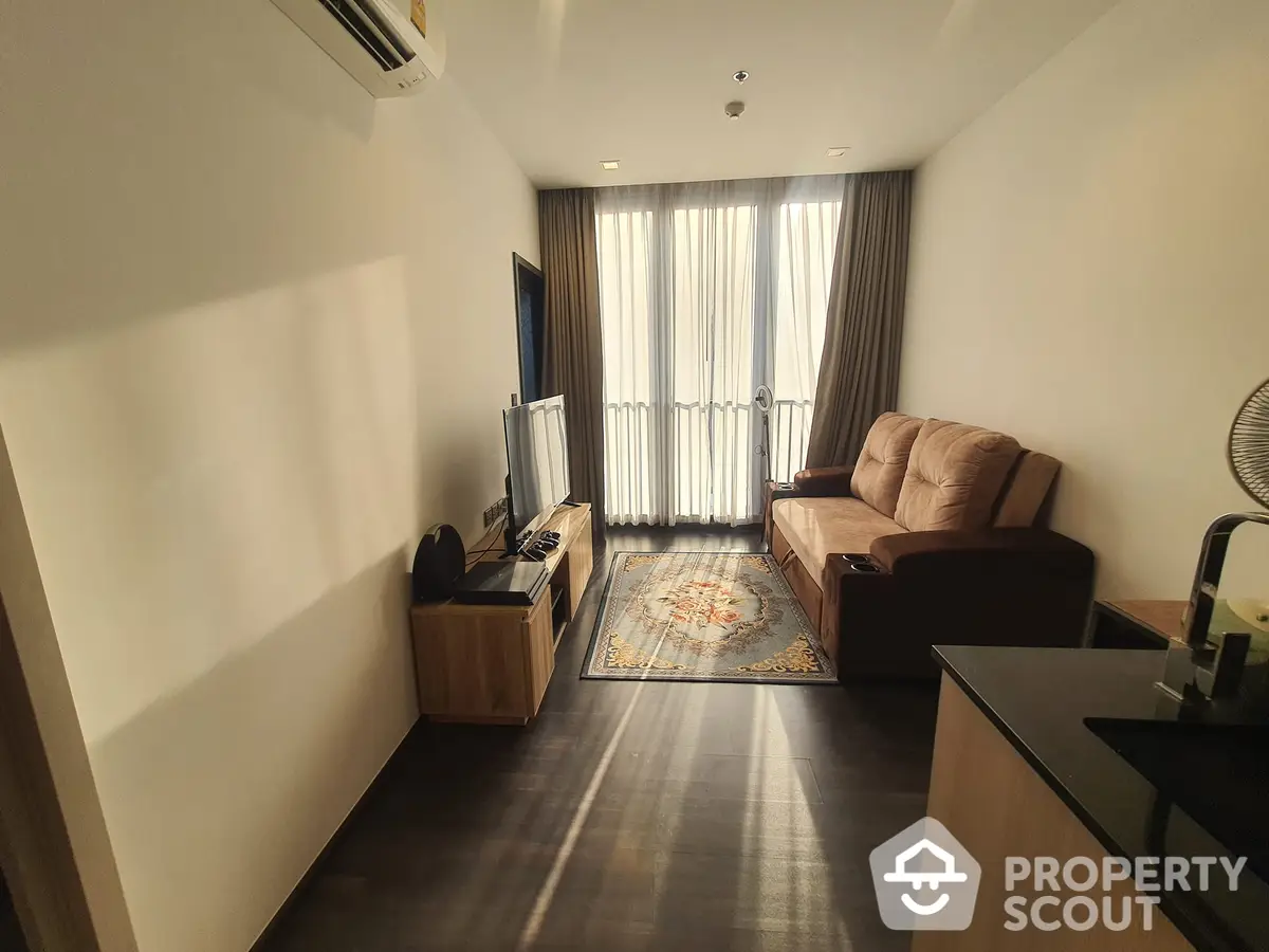 Spacious living room with natural light, elegant wooden flooring, comfortable sofa set, and access to a sunlit balcony, perfect for relaxation and entertainment.