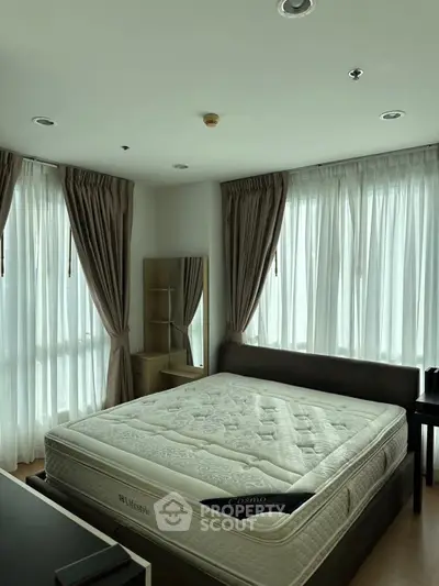 Spacious bedroom with large windows and natural light, featuring a comfortable bed and elegant curtains.