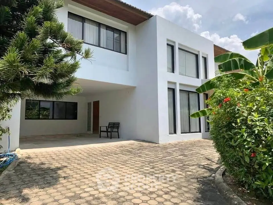 Modern two-story white house with large windows and lush garden