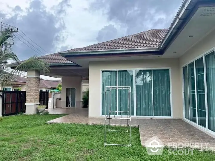 Charming single-story home with tiled patio and lush green lawn, featuring large sliding glass doors for natural light.